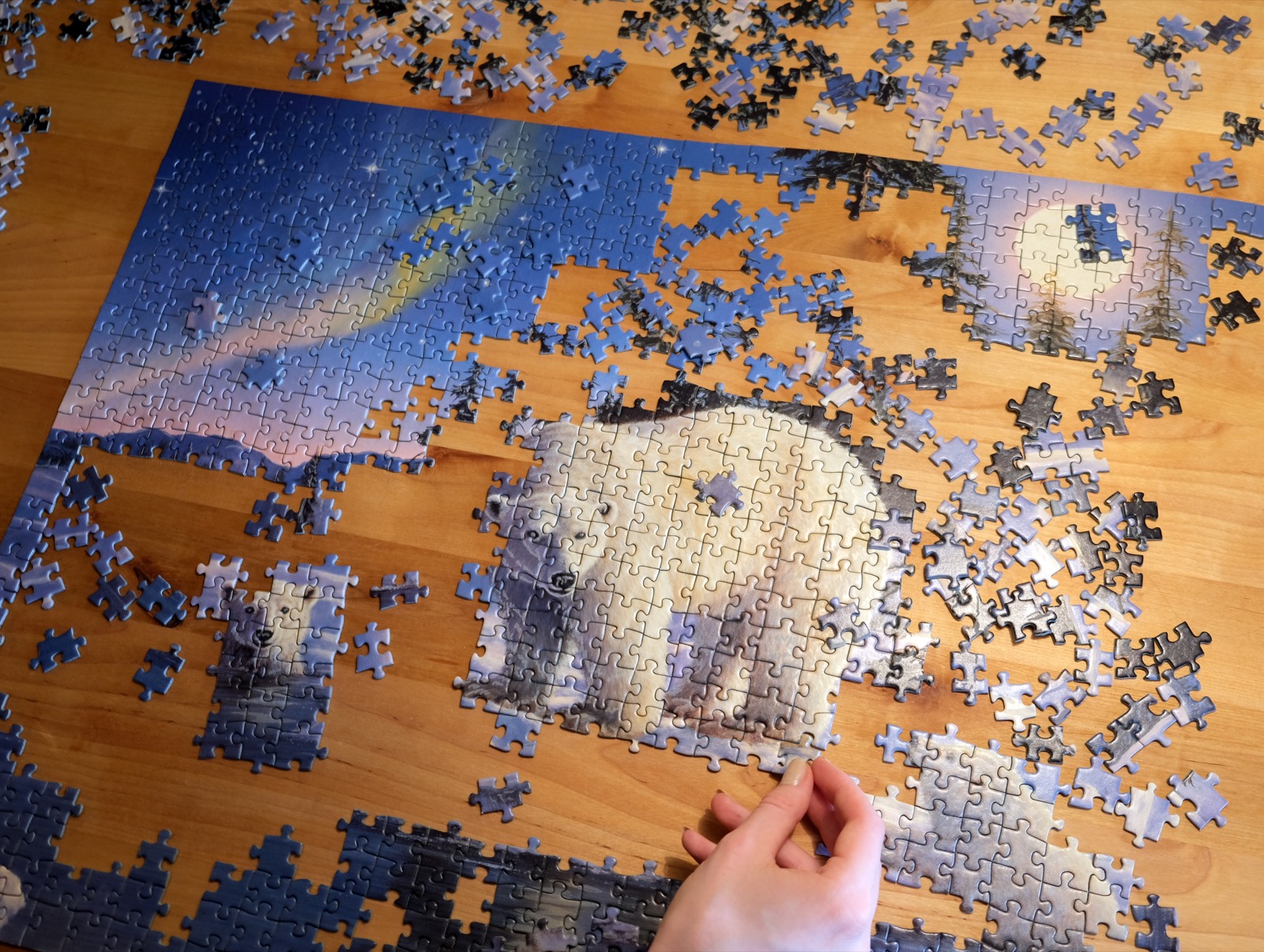 An adult's hands working on a jigsaw puzzle at a table. Puzzle pieces are sorted by color nearby, and a section of the image is partially assembled. The focused, quiet activity captures the flow state that psychologists associate with jigsaw puzzling.